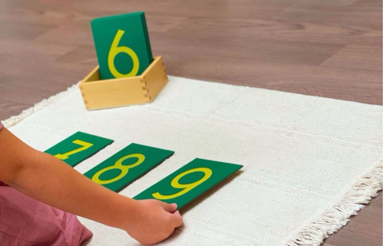 Une main d'enfant pose les chiffres rugueux 7, 8 et 9 sur un tapis